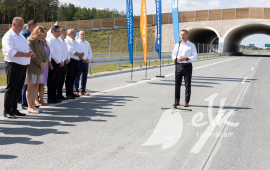 Prezydent Ełku przemawia na drodze Via Baltica z boku stoją oficjalni goście. W tle most i drzewa